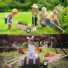 Children gardening with a pink wheelbarrow and wooden tools in a yard