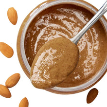 Glass bowl of creamy almond butter with a spoon and scattered almonds