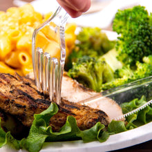 Clear fork and spoon serving cutlery on plated food with leafy greens