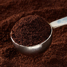 Dark roasted coffee grounds piled in a metal scoop