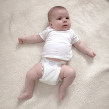 Baby wearing a white diaper over a soft surface, shown from the front