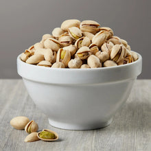 In-shell pistachios in a white bowl with a few pistachio shells nearby
