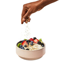 Hand sprinkling shelled hemp hearts into fruit-topped bowl
