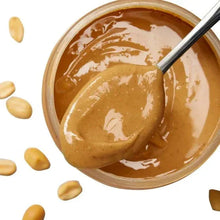 Creamy peanut butter in bowl with spoon and scattered peanuts