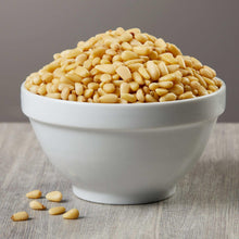 Pine nuts in a white bowl with a few kernels scattered nearby