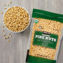 Pine nuts in a white bowl beside green organic pine nuts bag