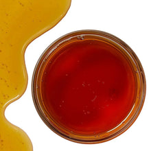 Glass jar filled with amber raw honey with a smooth, glossy surface.