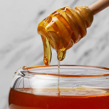 Amber honey stream dripping into a glass container.