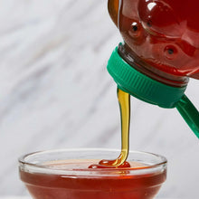 Bottle with green cap pouring amber honey into a glass bowl.