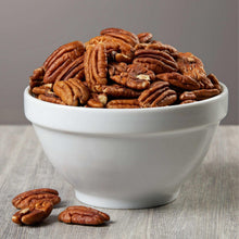 Pecan halves in a white bowl with scattered nut pieces