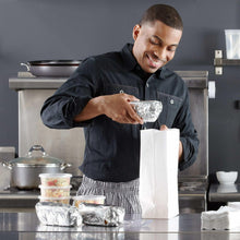 Chef holding a piece of aluminum foil over a work surface in a kitchen