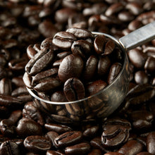 Whole bean coffee beans in a metal scoop on coffee grounds