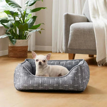 Gray fabric pet bed with wide bolster and curved opening, small dog sitting inside