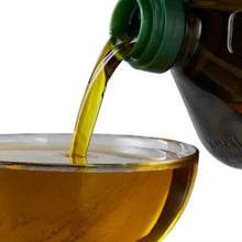Extra virgin olive oil pouring from green-capped bottle into a glass bowl