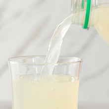 Glass of pale yellow lemonade with clear liquid pouring in