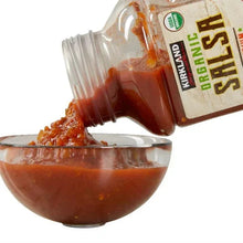 Organic salsa being poured from a jar into a bowl of red salsa
