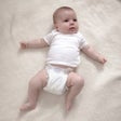 Infant wearing a white diaper, lying down with arms out