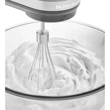 Hand mixer whisking white batter in a mixing bowl with spinning beaters.