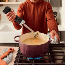 Cordless hand blender above a pot, blending shaft in thick mixture