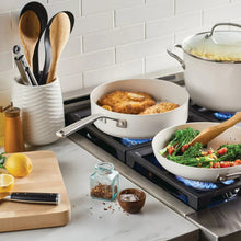 White nonstick pot with lid on stovetop, plus matching skillet and utensils