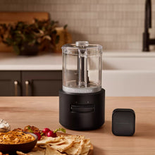 Food chopper on countertop with clear jar and black base, plus compact control