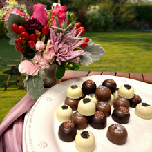 Chocolate truffles on white platter with cream and dark pieces beside flowers