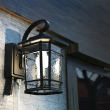 Black outdoor LED wall lantern with clear glass panels, mounted on a house wall