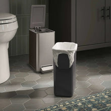 Black step trash can with open lid and pull handle area, standing in a bathroom.