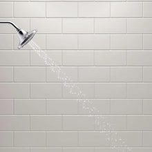 Chrome showerhead shower stream with water droplets on white tile