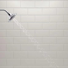 Water spray from chrome showerhead over tile wall