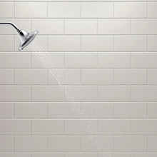 Water spray from chrome showerhead across tiled surface