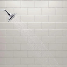 Water stream from chrome showerhead across tile wall
