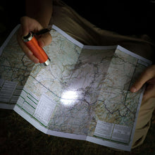 Multicolor LED flashlight in hand shining light over folded map