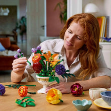 LEGO flower arrangement on a table with multicolor blooms while a person assembles it