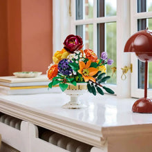 LEGO flower arrangement on a white pedestal stand with orange, purple, and yellow blooms