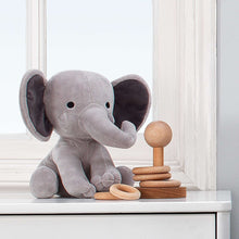 Gray plush elephant toy sitting and facing left, with floppy ears and trunk.