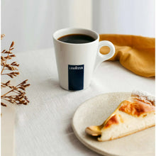 Lavazza espresso mug on table with yellow napkin and pastry slice