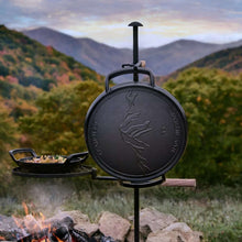 Le Creuset Alpine skillet on a stand with food inside, outdoors near open fire