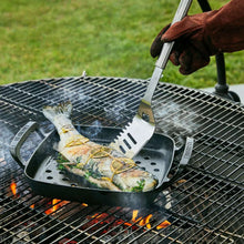Perforated square grill basket on a barbecue grate with fish and spatula