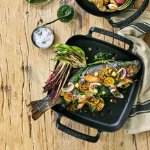 Black square grill basket with handles, filled with seafood and herbs