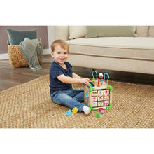 Wooden activity cube toy on a rug with number tiles and handle bars, played by toddler
