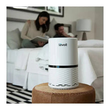 White Levoit air purifier on an ottoman, blue indicator light at the top