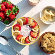 Bowl of yogurt topped with strawberries, banana slices, and multigrain cereal squares