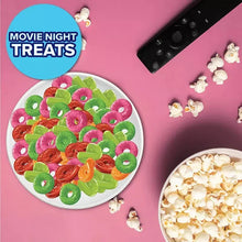 Bowl of colorful gummy rings in green, pink, and orange with popcorn pieces nearby