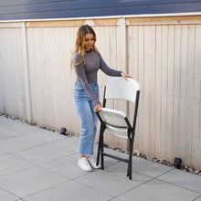 White folding chair held upright, folded black frame with white seat and back