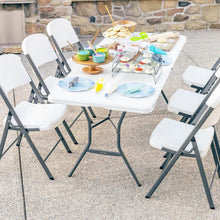 White outdoor folding table with black legs and surrounding chairs