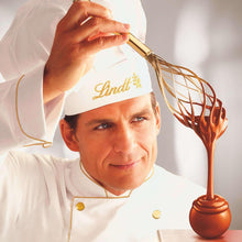 Lindt Lindor truffle held by chef in white coat with caramel-colored dipping chocolate