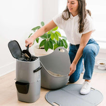 Cat litter disposal pail with black scoop handle being used near an open lid