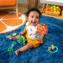 Baby holding orange and blue teething ball with crinkle rings and small toy pieces