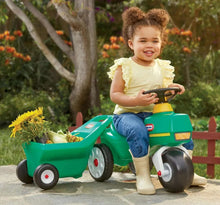 Green ride-on tractor with yellow seat and attached cart; toddler sitting and smiling